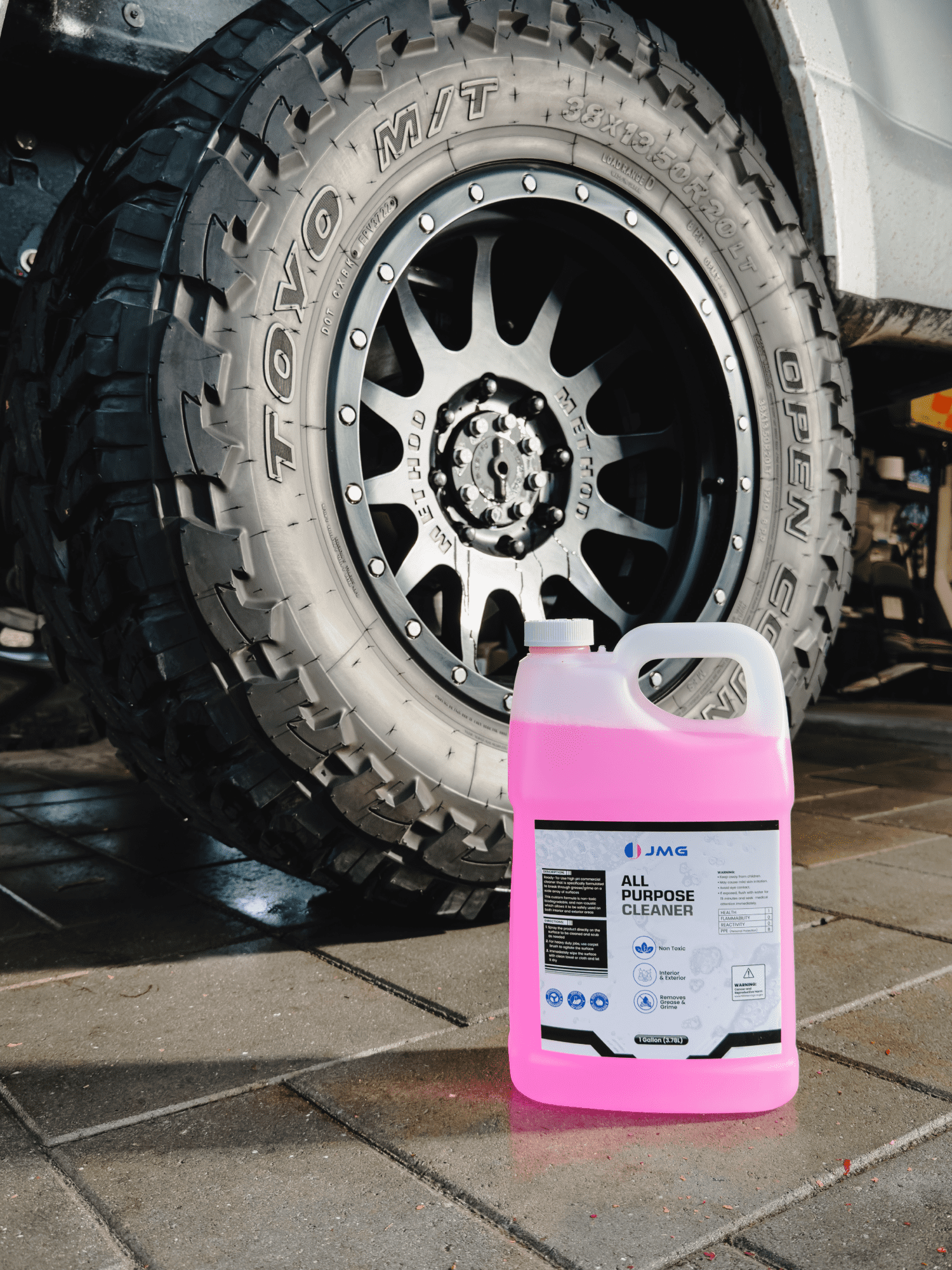 Case of 4 JMG All Purpose Cleaner gallons in front of freshly cleaned truck tire and rim at San Francisco fleet maintenance shop