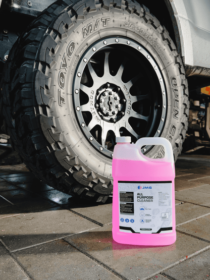 Case of 4 JMG All Purpose Cleaner gallons in front of freshly cleaned truck tire and rim at San Francisco fleet maintenance shop